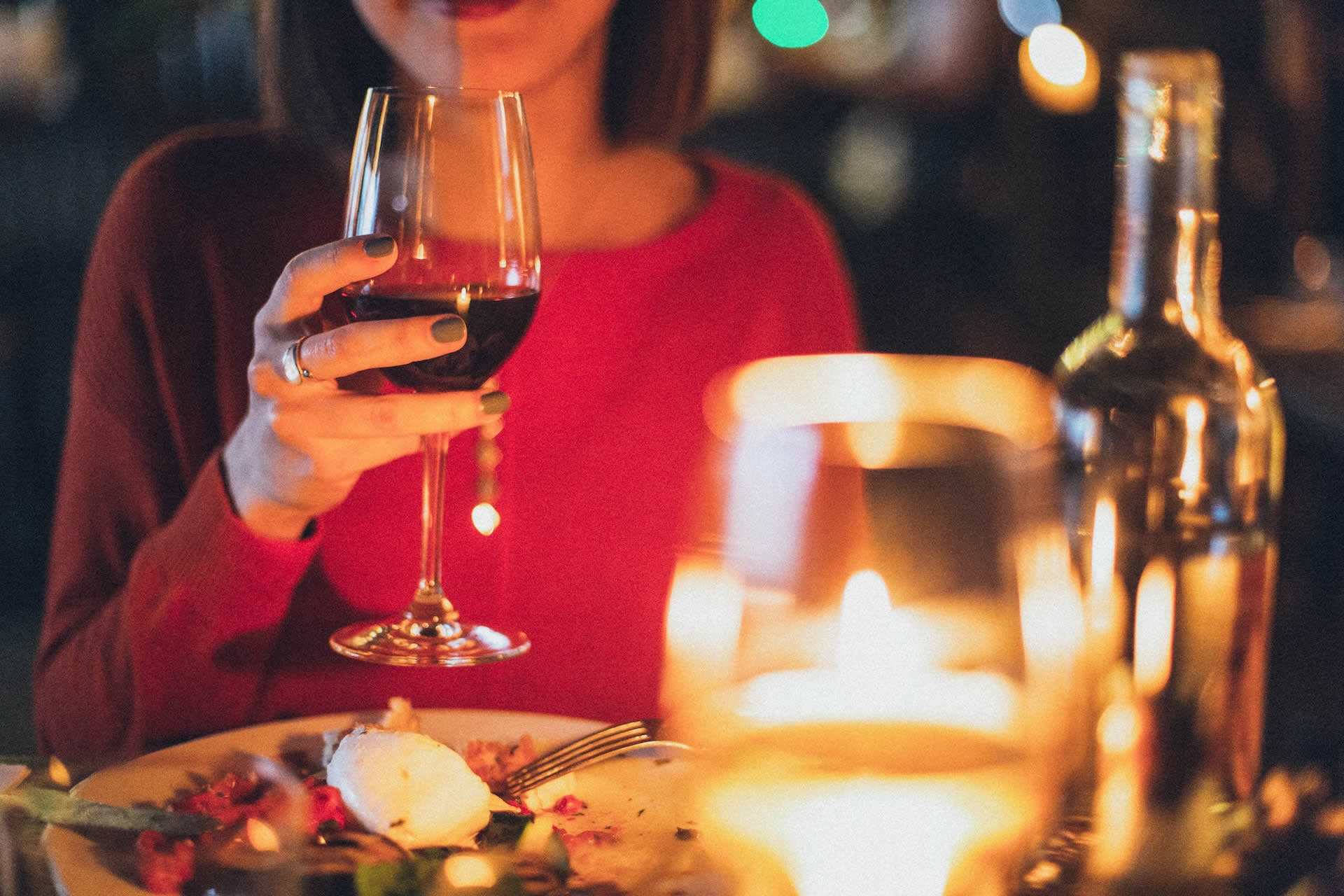 Woman holding a glass of red wine while enjoying a romantic dinner for two.