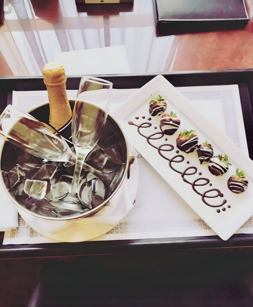 A bottle of champagne on ice next to a plate of chocolate-covered strawberries at The Emily Morgan Hotel.